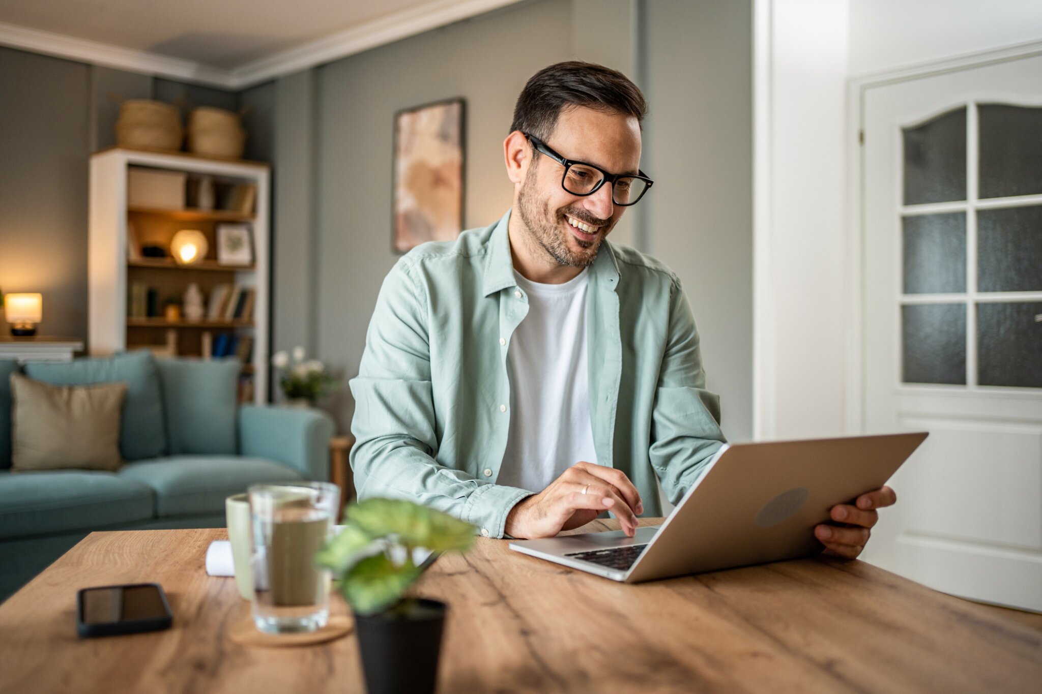A man sits at a desk smiling while working on a laptop.