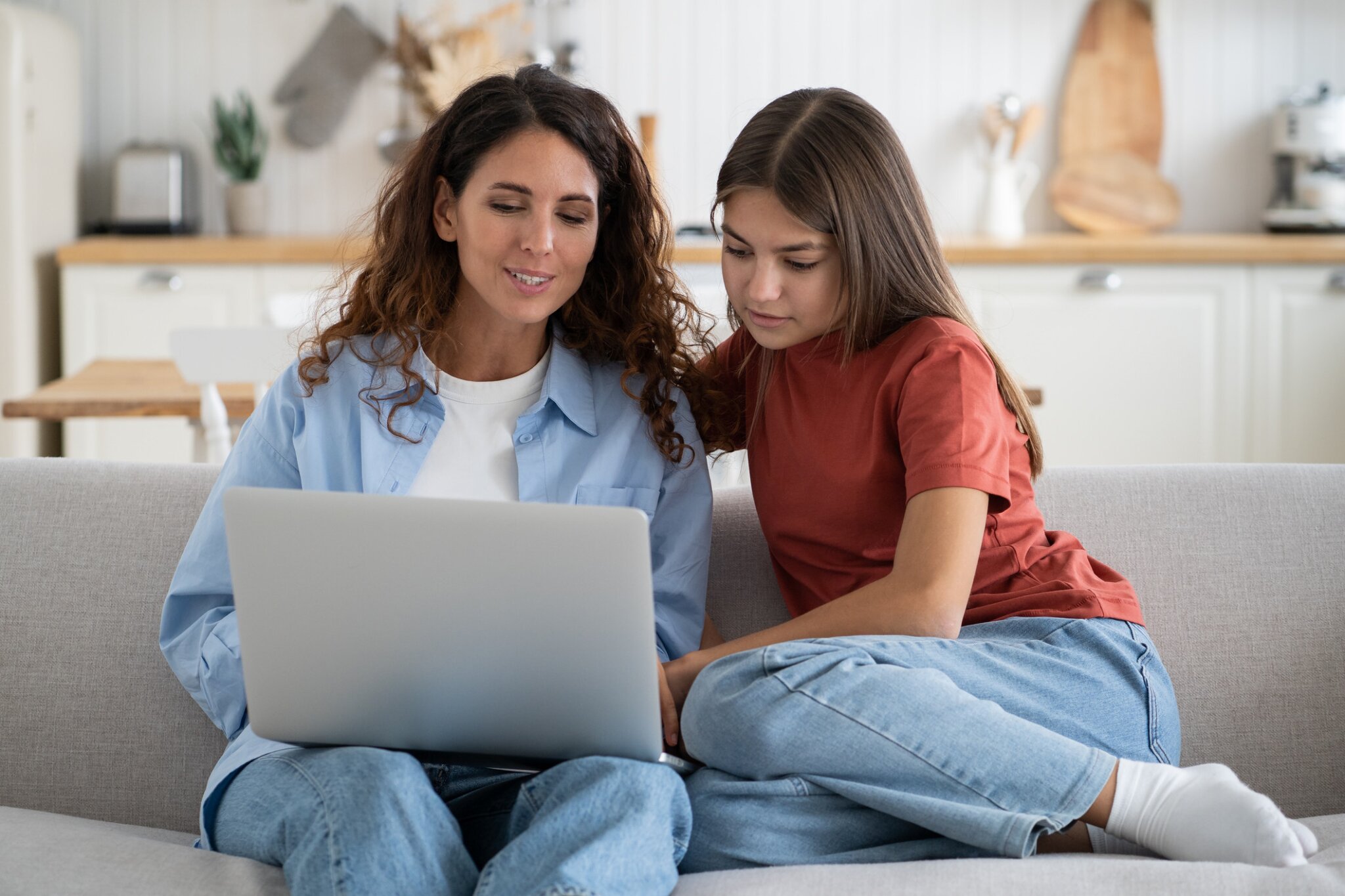 A mother and daughter collaborate on a laptop while sitting on a couch.