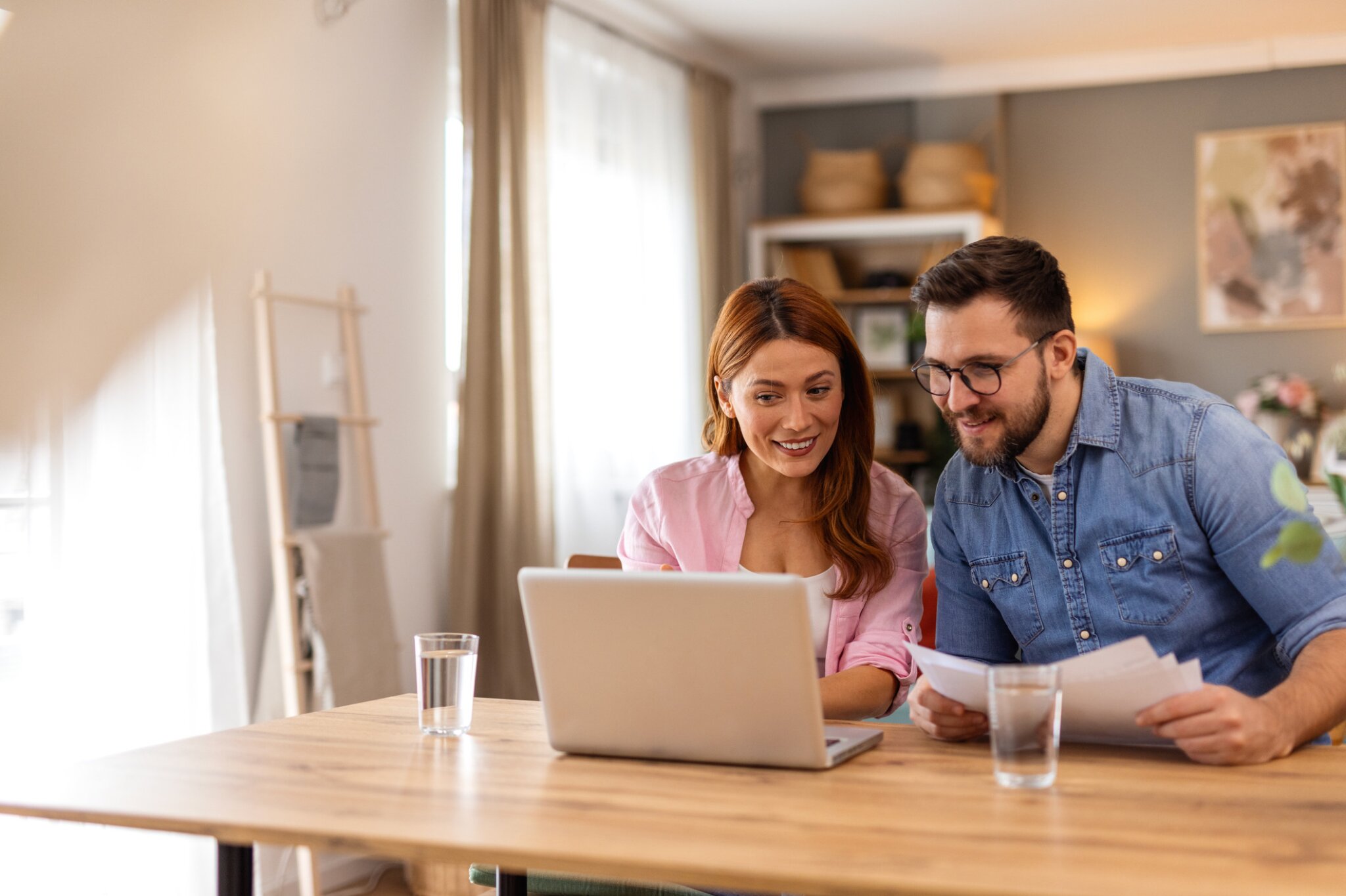 A couple sits at a desk working on a laptop.