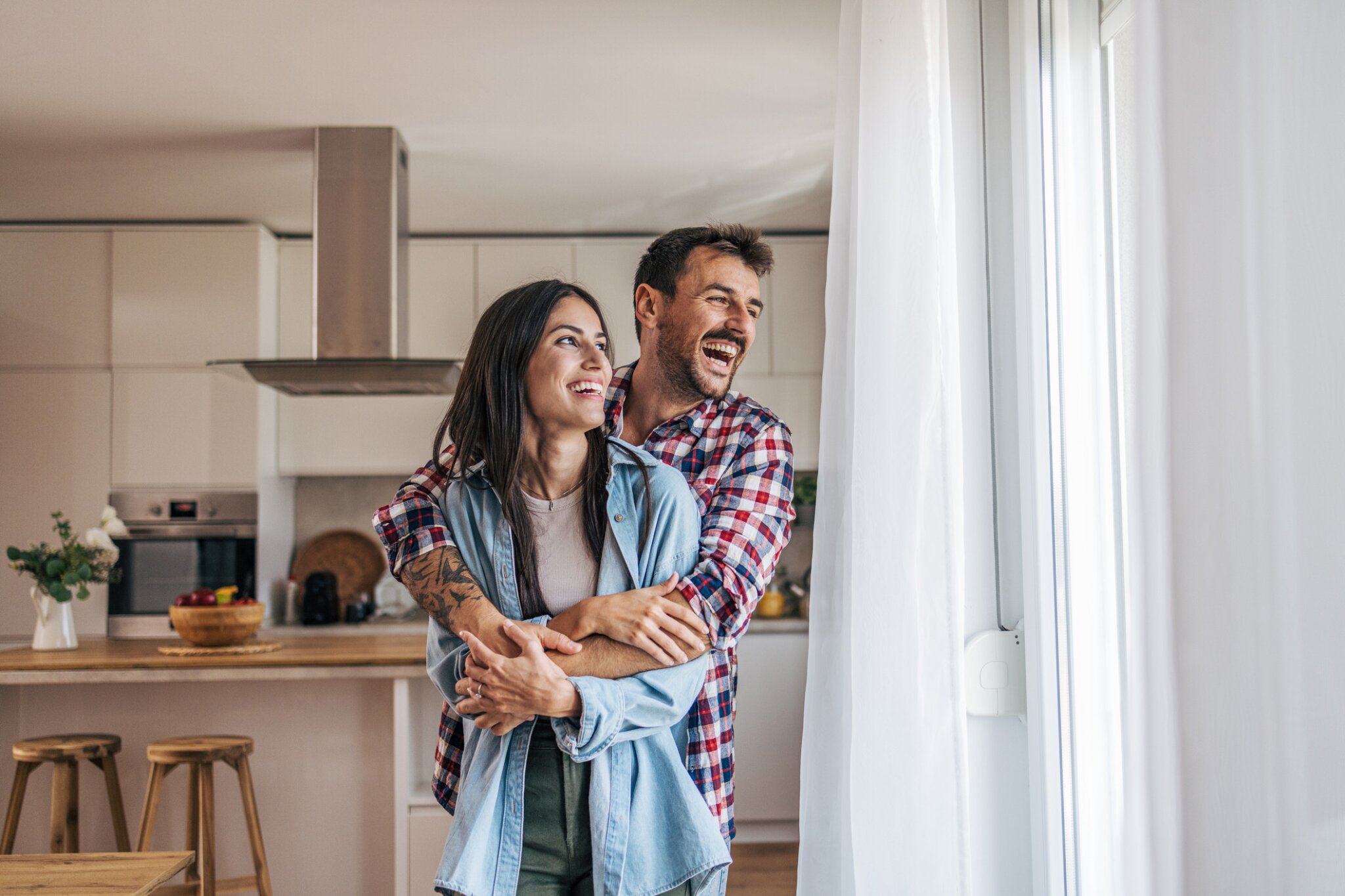 A couple stands in their kitchen hugging and smiling.