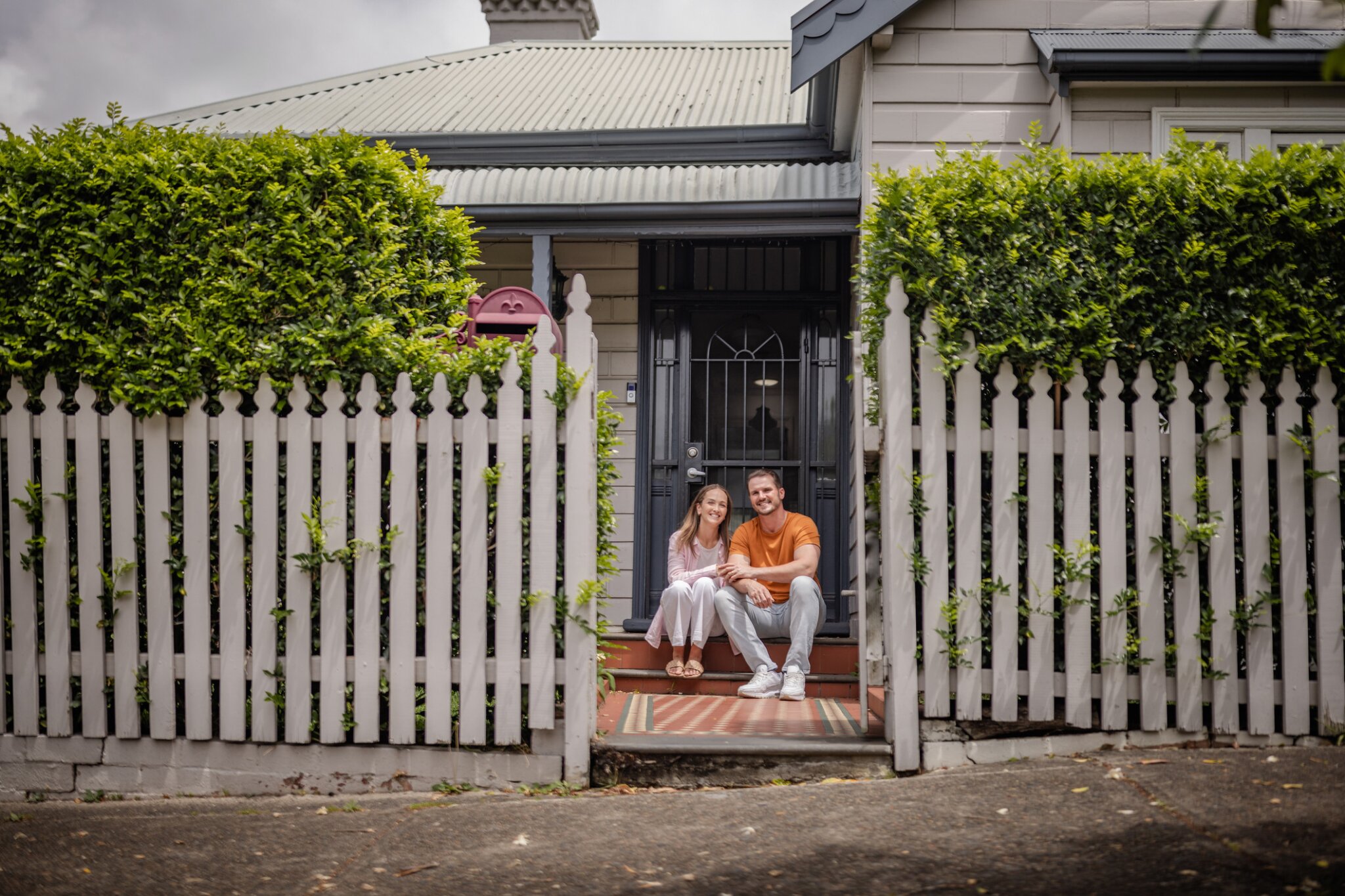 A couple sits on their porch holding hands and smiling.