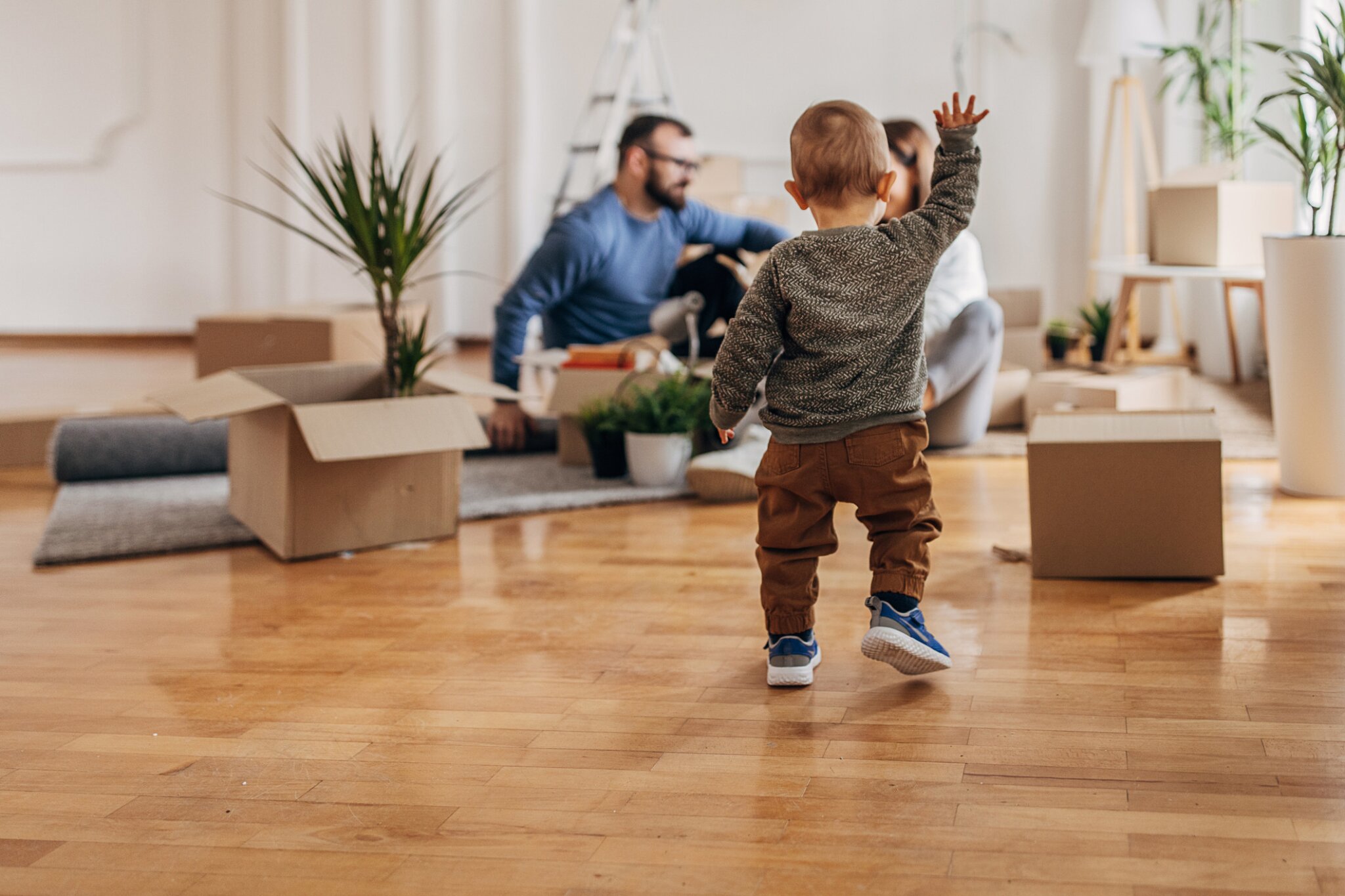 A toddler walks among moving boxes as a family unpacks.