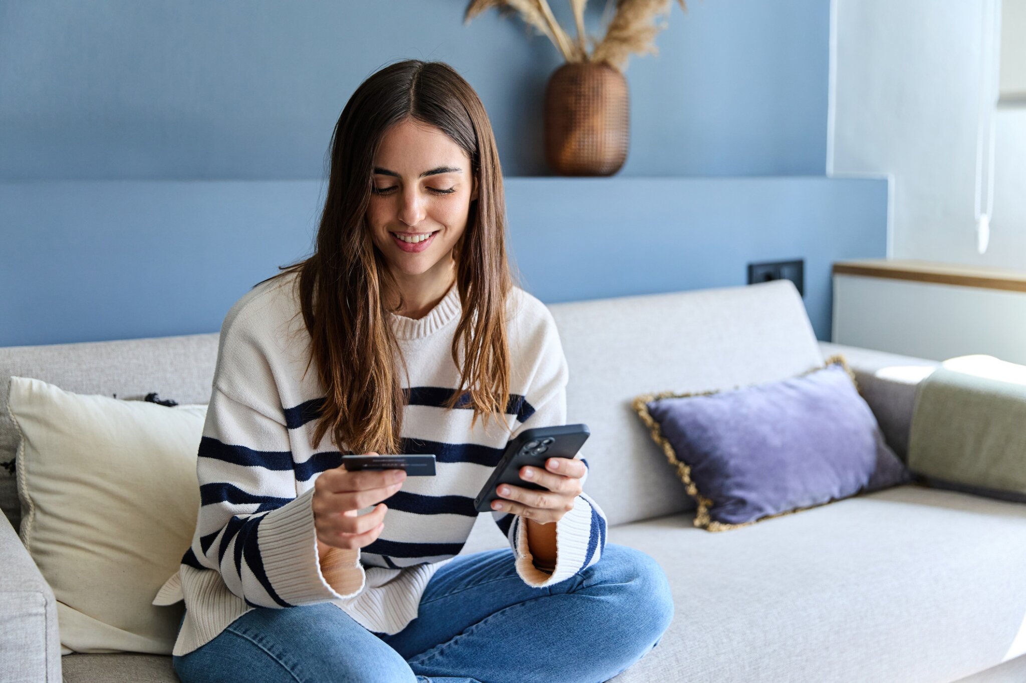 A woman sits holding a credit card and cellphone.