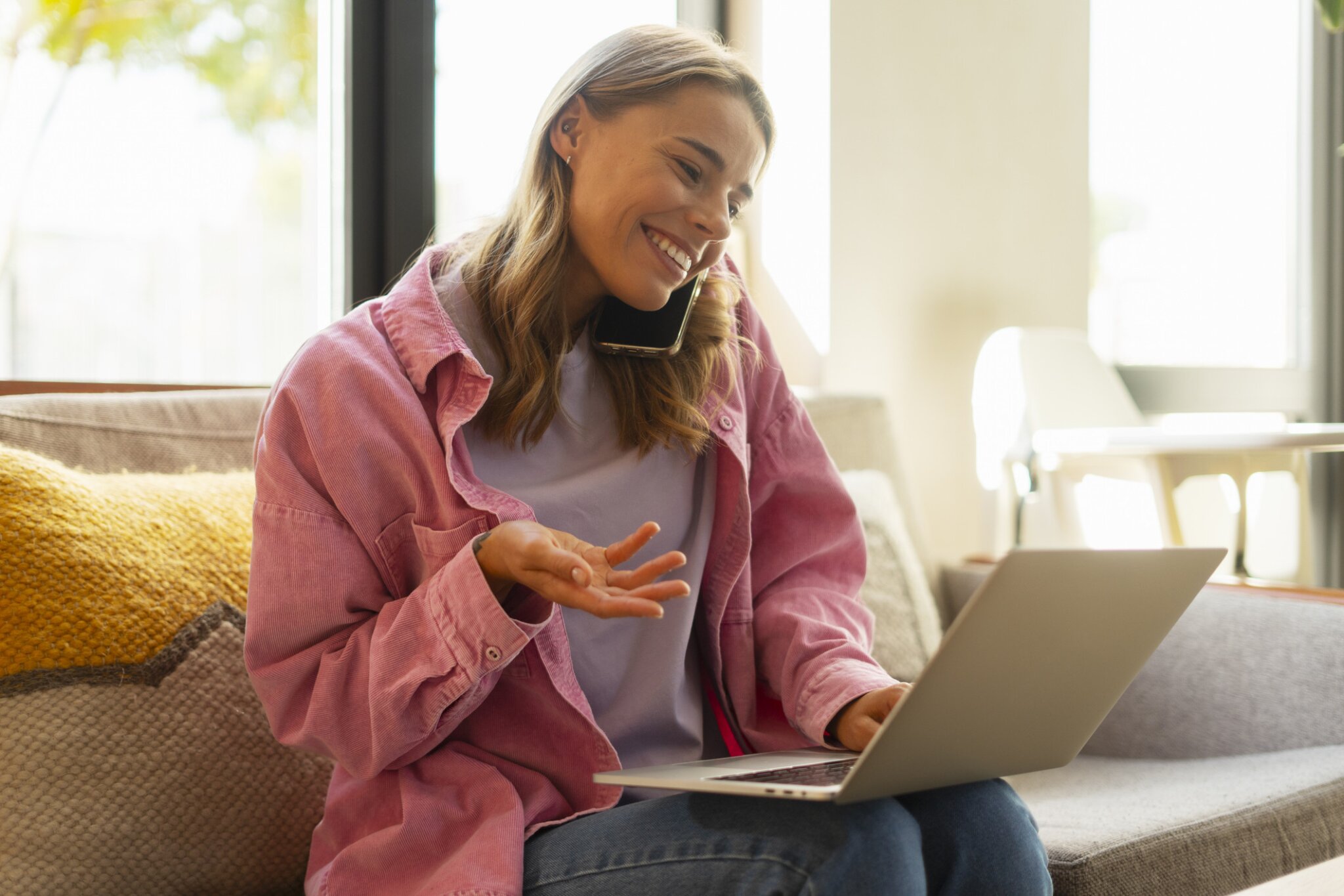 A woman talks on the phone while using a laptop.