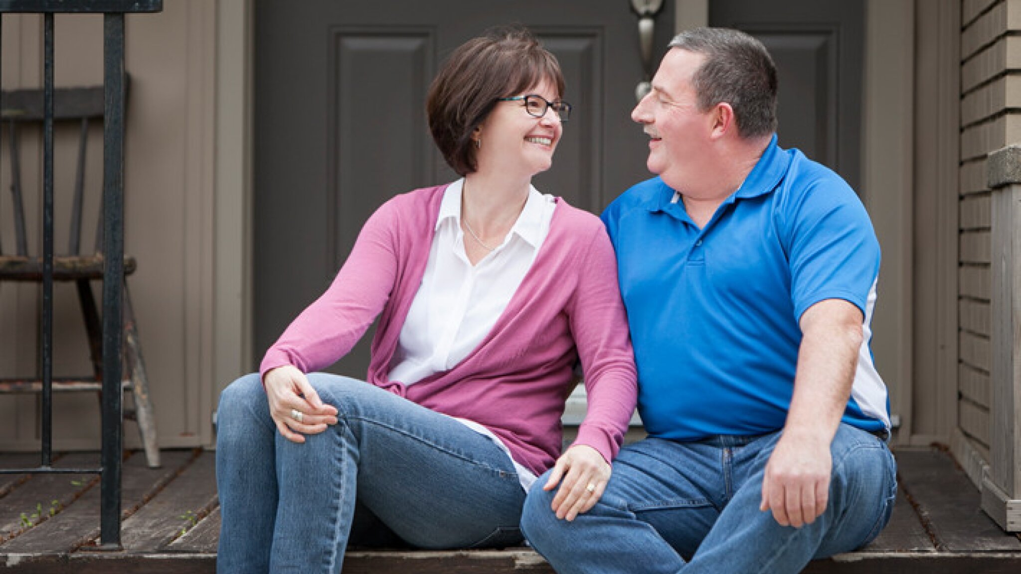 A couple smile at each other on a porch.