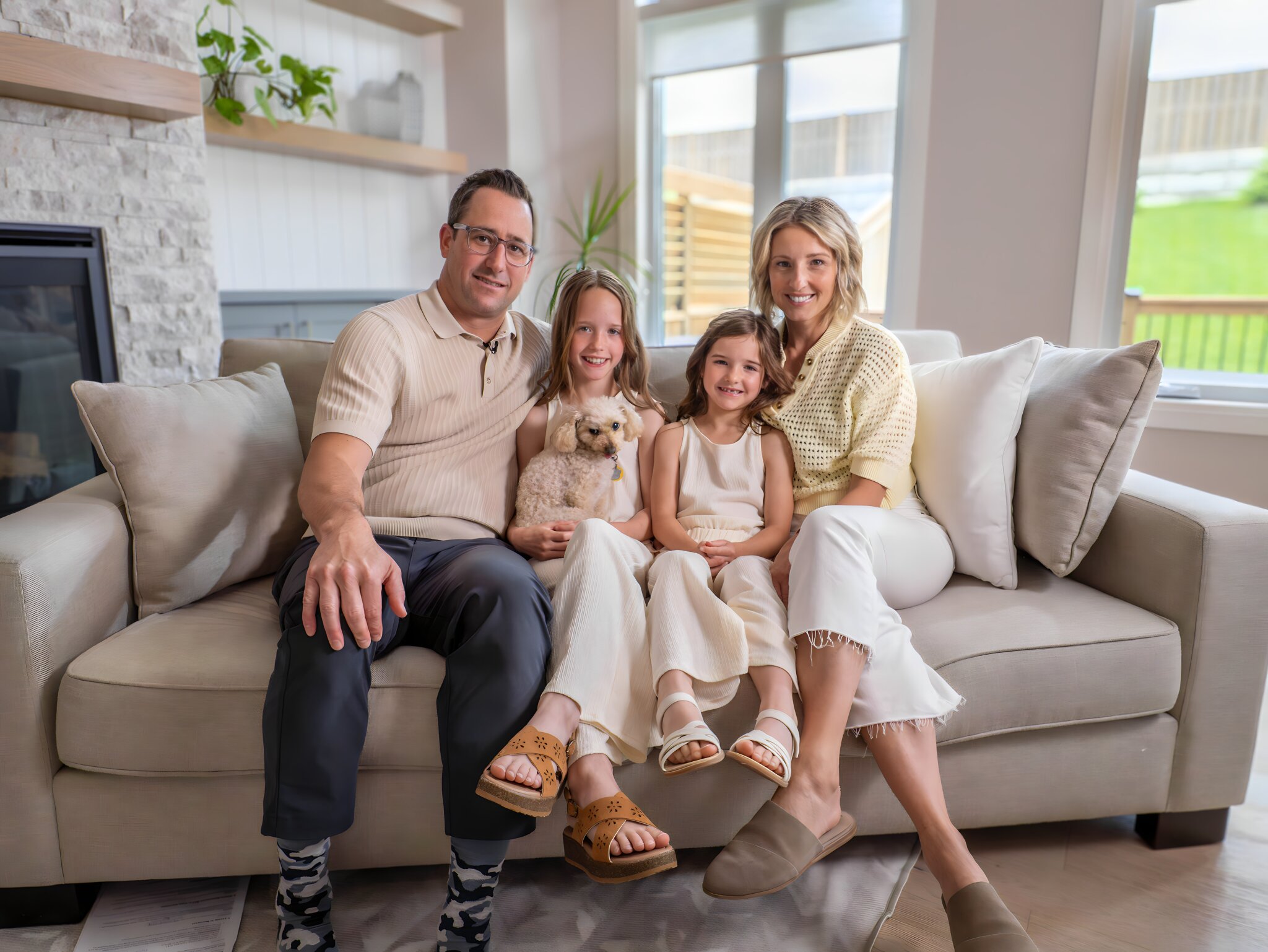 Family of four sitting on a couch with a small dog in a living room.