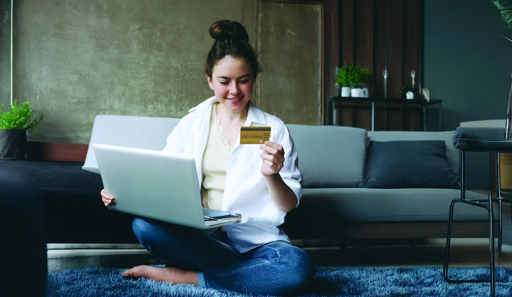 woman sitting on living room floor, using her laptop and credit card.